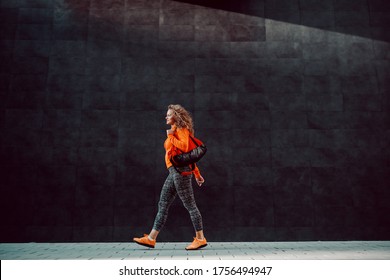 Full length of slim beautiful Caucasian woman in sportswear carrying bag while passing by gray wall. Gym time. - Powered by Shutterstock