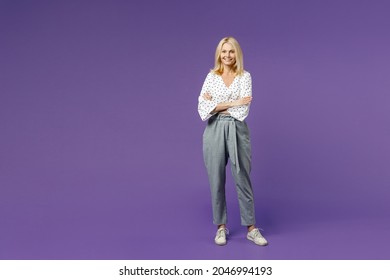 Full length of smiling attractive beautiful elderly gray-haired blonde woman lady 40s 50s in white dotted blouse holding hands crossed looking camera isolated on violet background studio portrait - Shutterstock ID 2046994193