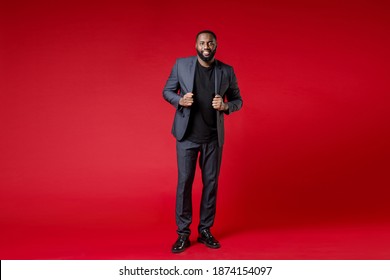 Full Length Of Smiling Attractive Confident Young African American Business Man 20s Wearing Classic Jacket Suit Standing Looking Camera Isolated On Bright Red Color Wall Background Studio Portrait