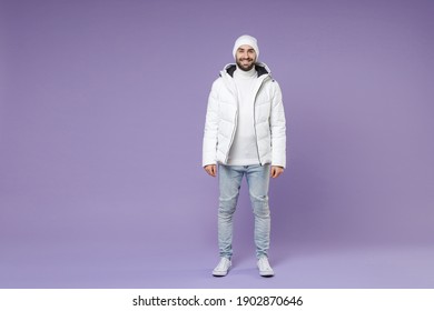 Full length of smiling attractive man in warm white padded windbreaker jacket hat standing looking camera isolated on purple background studio portrait. People lifestyle cold winter season concept - Powered by Shutterstock