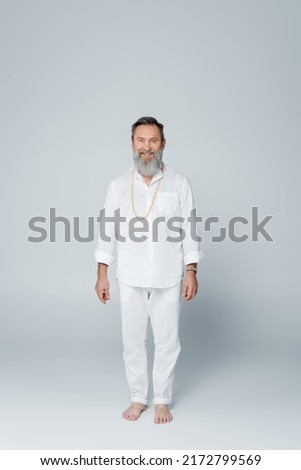 full length of smiling barefoot guru man in white clothes standing on grey