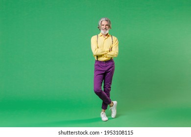 Full Length Of Smiling Elderly Gray-haired Mustache Bearded Man Wearing Casual Yellow Shirt Suspenders Holding Hands Crossed Looking Camera Isolated On Bright Green Colour Background, Studio Portrait