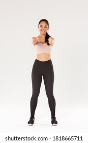 Full length of smiling good-looking and slim asian fitness coach, female athlete in activewear showing workout equipment, holding resistance stretching band, perform exercises, white background - Shutterstock ID 1818665711