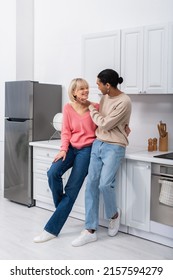 Full Length Of Smiling Multiethnic Couple Looking At Each Other In Modern Kitchen