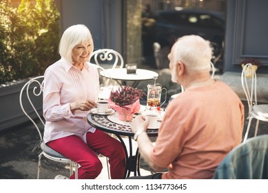 Full length of smiling old lady sitting at table and drinking tea with man. They are facing each other and looking with love and admire - Powered by Shutterstock