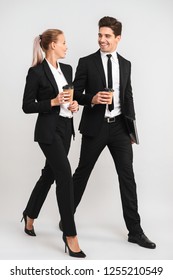 Full Length Of Smiling Young Business Couple Walking Isolated Over Gray Background, Holding Cups Of Takeaway Coffee