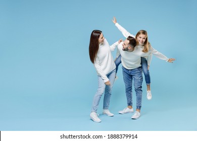 Full Length Of Smiling Young Parents Mom Dad With Child Kid Daughter Teen Girl In Sweaters Giving Piggyback Ride To Joyful, Sitting On Back Isolated On Blue Background. Family Day Parenthood Concept