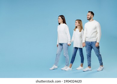 Full Length Of Smiling Young Parents Mom Dad With Child Kid Daughter Teen Girl In White Sweaters Holding Hands Walking Going Isolated On Blue Background Studio Portrait. Family Day Parenthood Concept