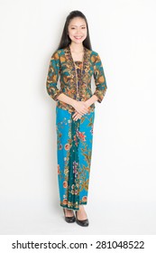Full Length Southeast Asian Girl In Batik Dress Standing On Plain Background.