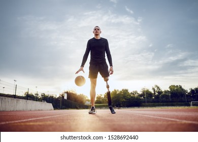 Full length of sporty caucasian handicapped man in sportswear and artificial leg dribble the ball while standing on racetrack. - Powered by Shutterstock