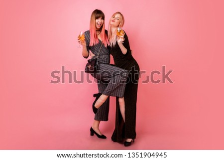 Full length studio  image of celebrating women in party dress drinking shampagne and have great time together. Pink background. Happy emotions.