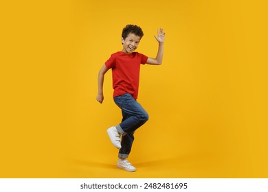 Full length studio portrait of beautiful happy smiling African American child dancing and waving with his hand, isolated over bright colored orange yellow background.                                - Powered by Shutterstock