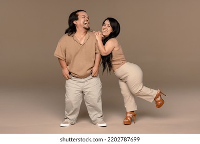 Full Length Studio Portrait Of A Hispanic Man In His 50s And A Hispanic Woman In Her 20s Posed Laughing Smiling On A Neutral Background, Both With Dwarfism