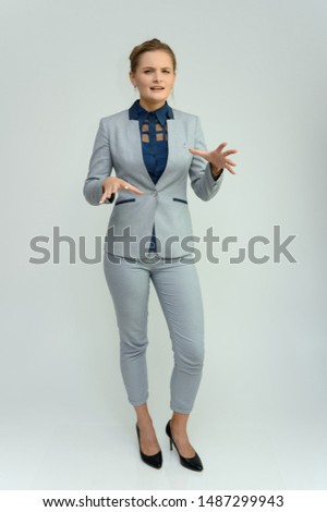Full length studio portrait of a pretty young woman girl in a business suit on a white background. He stands right in front of the camera, explains, shows hands with emotions.