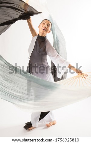 Full length studio shot of active female dancer in black and white layers, dancing with long fabric fans.