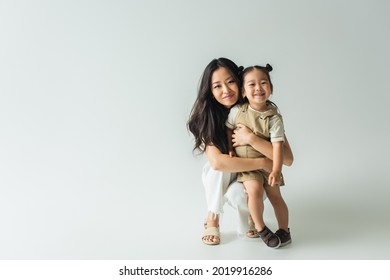 full length of stylish asian mother hugging toddler daughter on grey - Shutterstock ID 2019916286