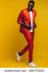 Full length of stylish young african man in orange outfit over yellow background. Fashion model in smart casuals.