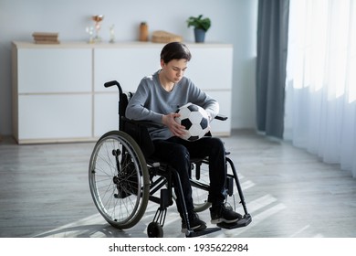 Full Length Of Teen Football Player In Wheelchair Holding Soccer Ball And Feeling Stressed Over His Injury At Home