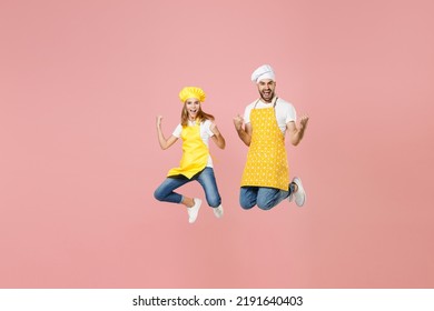 Full Length Teen Fun Girl Dad Father's Helper Chef Cook Confectioner Baker In Yellow Apron Cap Jump High Doing Winner Gesture Clench Fist Celebrating Isolated On Pastel Pink Background Studio Portrait