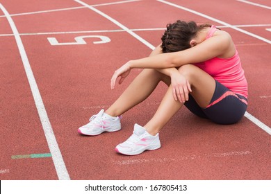 Full length of a tensed sporty woman sitting on the running track - Powered by Shutterstock