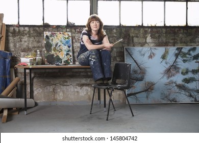 Full length of thoughtful young female artist with paintings in workshop - Powered by Shutterstock