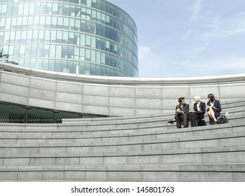 Full Length Of Three Business People Sitting On Steps Outside Office Building During Lunch Break