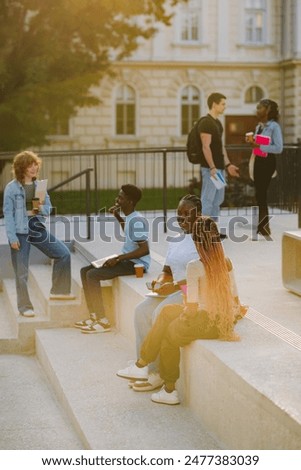 Full length of three groups of multicultural college students sitting and standing on staircase at university campus and chatting during coffee break between lectures.In background is college building