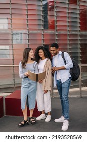 Full length of three young diverse classmates checking their homework before lessons outside. Brunette guy and girls wear casual clothes. Knowledge concept - Shutterstock ID 2193528569