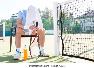 Full length of tired mature man with covered head sitting on chair by net at tennis court on sunny day - Powered by Shutterstock