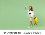 Full length traveler tourist woman in casual clothes hat hold suitcase do selfie on mobile cell phone isolated on pastel green background. Passenger travel abroad weekends. Air flight journey concept