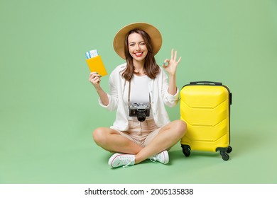 Full length traveler tourist woman in casual clothes hat hold suitcase passport sit ticket ok gesture isolated on green background Passenger travel abroad weekends getaway Air flight journey concept