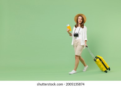 Full length traveler tourist woman in casual clothes hat hold yellow suitcase passport tickets go isolated on green background. Passenger travel abroad on weekends getaway. Air flight journey concept