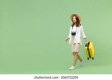 Full Length Traveler Tourist Woman In Casual Clothes Straw Hat Hold Yellow Suitcase Walk Go Isolated On Pastel Green Background. Passenger Travel Abroad Weekends Getaway. Air Flight Journey Concept