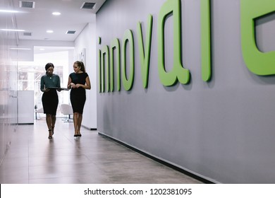 Full length of two business women walking through office hallway. Female coworkers walking in office corridor. - Powered by Shutterstock