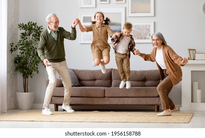 Full Length Of Two Excited Kids Siblings Having Fun Playing With Active And Positive Grandparents In The Living Room At Home, Enjoying Weekend Time With Energetic Senior Old Grandma And Grandpa