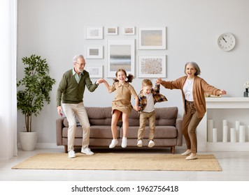 Full Length Of Two Excited Kids Siblings Having Fun Playing With Active And Positive Grandparents In The Living Room At Home, Enjoying Weekend Time With Energetic Senior Old Grandma And Grandpa