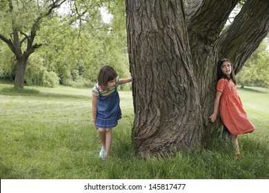 Full Length Of Two Girls Playing Hide And Seek By Tree