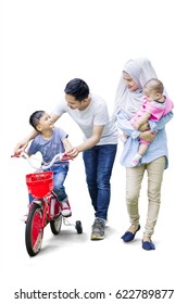 Full Length Of Two Muslim Parents Teach Their Son To Ride A Bicycle While The Mother Holding Her Baby