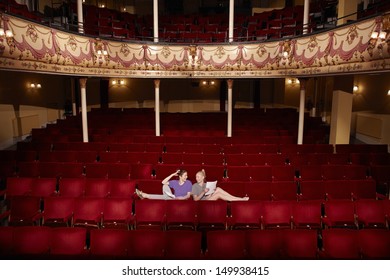 Full Length Of Two Young Women Sitting In Theatre Stall With Scripts