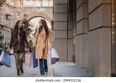 Full length of two young women girlfriends walking on the city street with shopping bags after buying purchasing fashion clothes, Christmas presents on sales offers discounts - Powered by Shutterstock