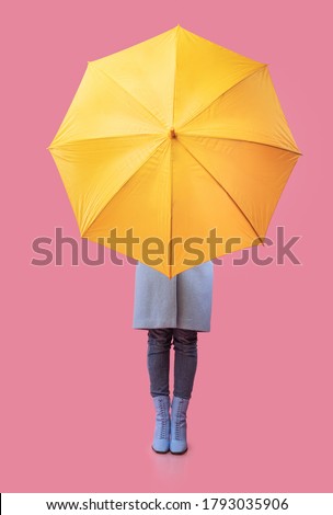 Full length of unrecognizable model in autumn clothes hiding behind yellow umbrella, vertical studio shot