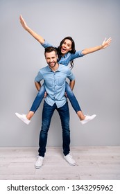Full length vertical body size photo funky cheer she her he him his lady guy piggyback ride walk meet adventures hands arms spread up wear casual jeans denim shirts clothes isolated grey background