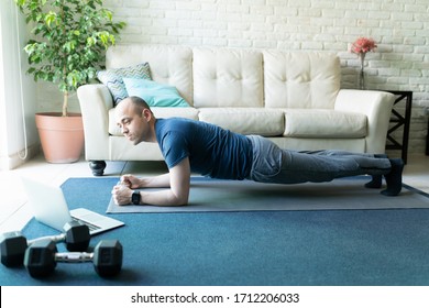 Full Length View Of An Active Caucasian Man Holding A Plank Pose While Looking At An Online Workout On A Laptop At Home