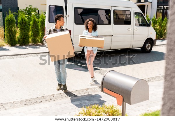 full length view of african
american man and woman holding boxes and looking at each
other