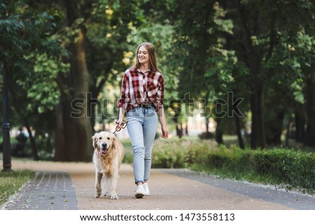 full length view of beautiful girl in casual clothes waking in park with golden retriever