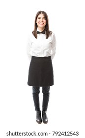 Full length view of a beautiful Hispanic waitress wearing an apron and a bowtie and smiling;
