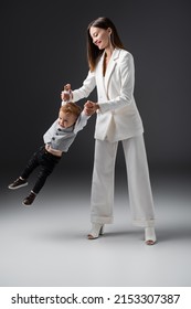 Full Length View Of Cheerful Woman Holding Hands Of Son While Lifting Him On Grey