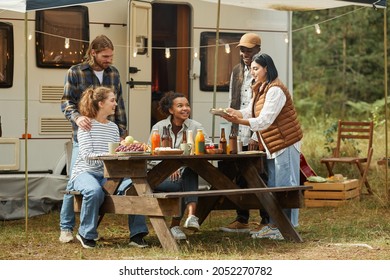 Full Length View At Diverse Group Of Young People Enjoying Picnic Outdoors While Camping With Trailer Van