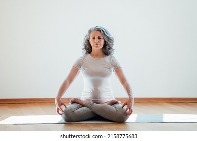 Full length view of the elderly woman practicing yoga at lotus pose in studio. Mature yoga teacher is take time for herself at home - Powered by Shutterstock