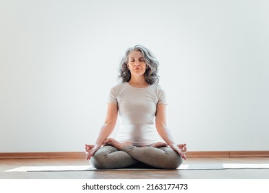 Full length view of the elderly woman practicing yoga at lotus pose in studio. Mature yoga teacher is take time for herself at home - Shutterstock ID 2163177473